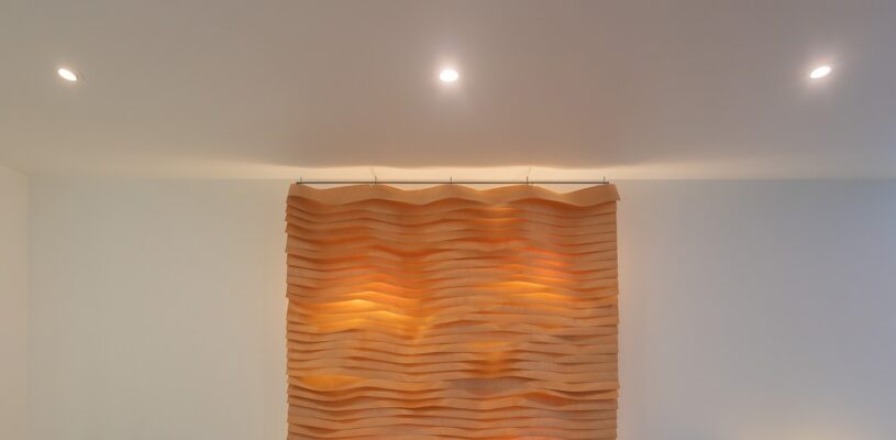 Olohuoneessa-kaunis-pari-seinavaloteoksesta-ja-uppospoteista_LedStorefi_ - LedStore LedStore.fi verkkokauppaan sopivasti muotoiltu kuvaus: Valkoisella seinällä moderni taideteos, joka päästä aaltomaisesti muotoilluista muotoilluista. Pehmeä valaistus teoksen tekstiuuria ja LED-kattovalot luovat lämpimän hehkun yläpuolelta.