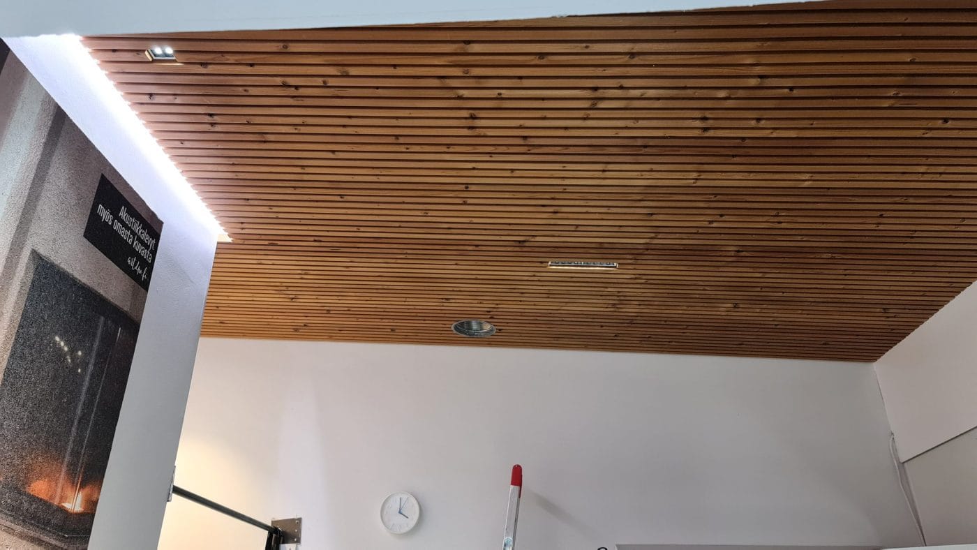 Puupaneloitu katto on varustettu upotetulla LED-valaistuksella ja pienellä ilmanvaihtoritilällä. Seinäkello ja osa takasta ovat näkyvissä, kun taas punakahvainen harja nojaa valkoista seinää vasten. Sopivaisia LED-valaisimet löydät helposti helposti LedStore.fi-verkkokaupasta!