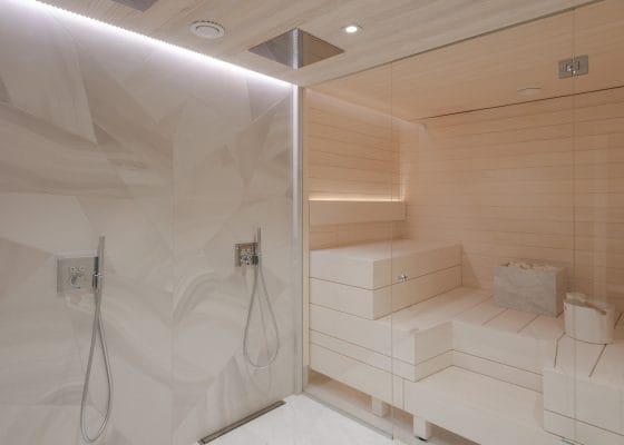 Ylellinen kylpylä, jossa on sauna, puiset penkit, geometriset laattasuihkut ja kiillotettu lattia, joka valaisee pehmeästi ympäristön LED-valaistuksella rentouttavan tunnelman luomiseksi.