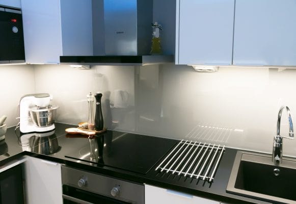 Moderni keittiö, jossa LED-valaistu musta työtaso, ruostumattomasta teräksestä valmistetut kodinkoneet, valkoiset kaapit, sekoitin, pippurimylly, öljypullo tiskillä.