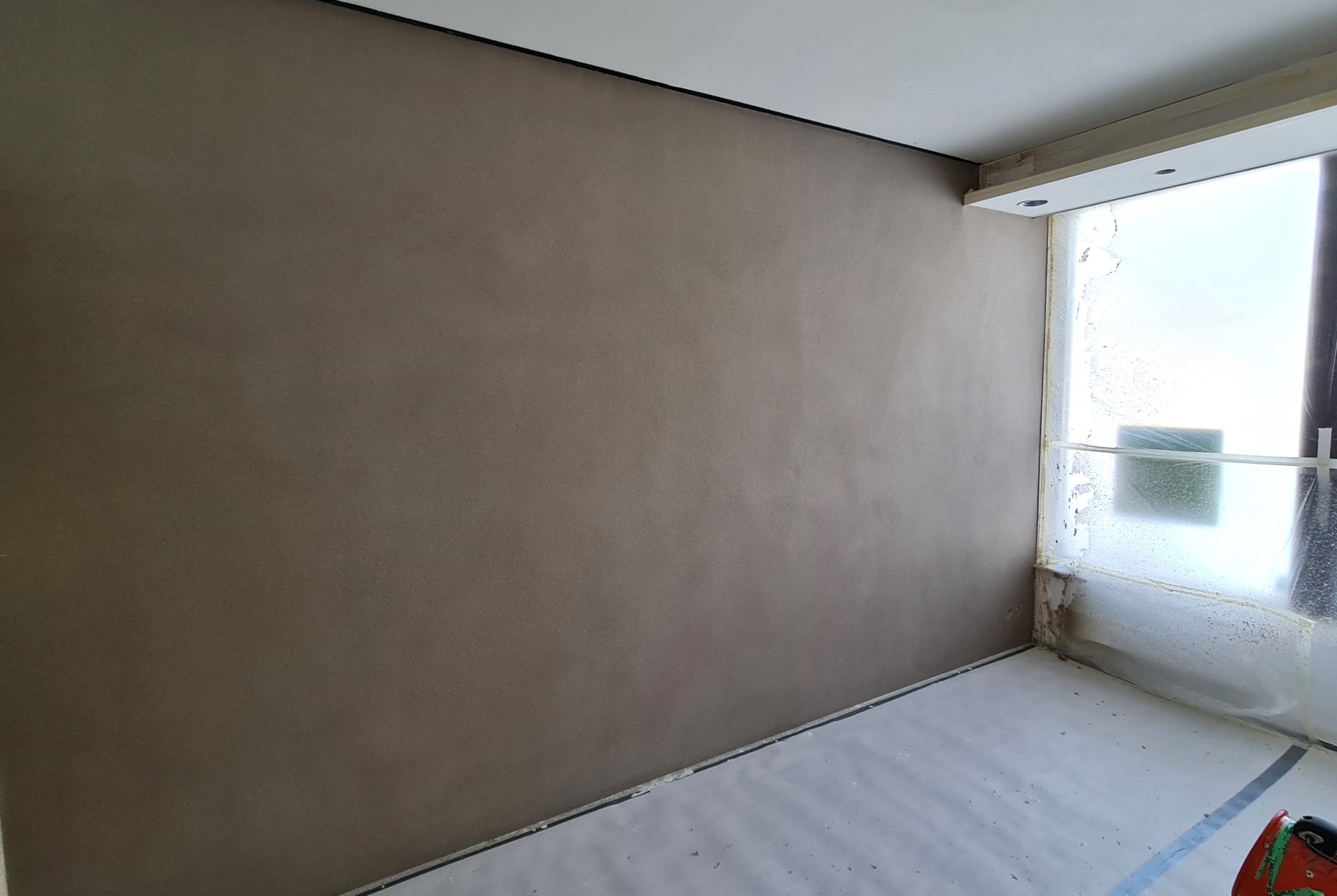 Liipattu seinä kuivatetaan - LedStore Tuoreesti maalattu, beige seinä kylpe LED-valojen luomassa luonnollisessa valossa, joka on suurista lattiasta kattoon ulottuvista ikkunoista. Ikkunat on suojattu muovikelmulla, ja lattia on peitetty suojakankaalla maalaustöiden ajaksi.
