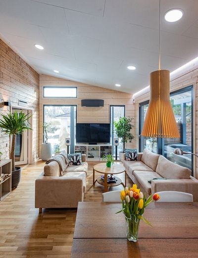 Modernes Wohnzimmer mit großen Fenstern, beigen Sofas, TV, Pflanzen, Holztisch mit Tulpenvasen, Holztafelwänden - beleuchtet mit stilvoller LED-Beleuchtung.
