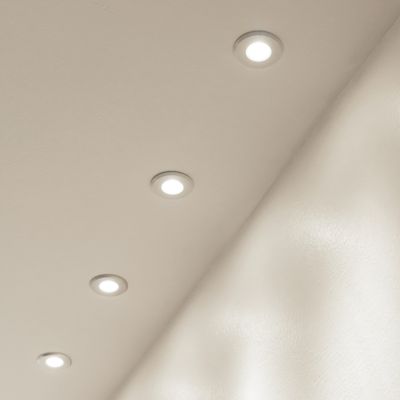 Eine Decke mit vier kreisförmigen LED-Einbauleuchten, die gleichmäßig verteilt sind und ein sanftes Licht auf einer flachen, hellen Oberfläche erzeugen. Eine energieeffiziente Beleuchtungsoption.