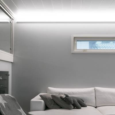 Ein minimalistisches Wohnzimmer mit natürlichem Licht, Fenstervorhängen und sanfter LED-Beleuchtung auf grauen Wänden.