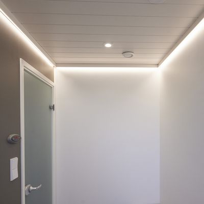 Ein minimalistischer Korridor mit Milchglastür, eleganten weißen Wänden, Holzdecke, Einbauleuchten und dezenten LED-Leuchtstreifen an den Rändern.