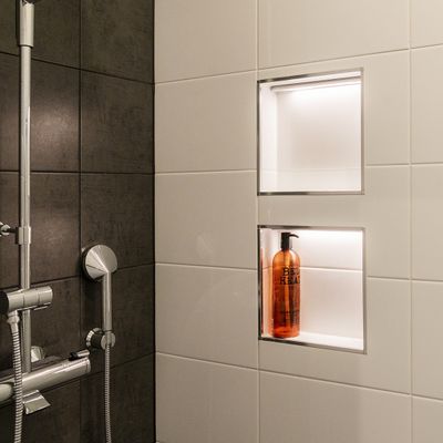 Moderne Dusche mit eingebautem LED-Licht, weiße und dunkelgraue Fliesen, elegante Chrom-Armatur, Shampoo-Flasche. Effektive Beleuchtung für stilvolle Bäder.
