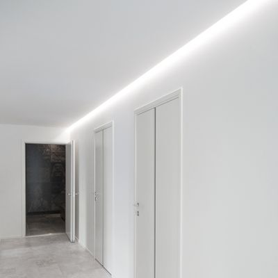 Korridor mit weißen Wänden und Türen, sanfte LED-Beleuchtung. Ein dunkler Durchgang am Ende unterstreicht das minimalistische Design.