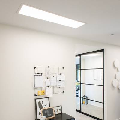LED-Deckenleuchten für das Büro beleuchten einen modernen Arbeitsbereich mit einer Glastrennwand und einer Wandtafel.