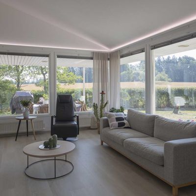 Modernes Wohnzimmer mit LED-Deckenleuchten, Stehlampe, natürlichem Licht aus großen Fenstern, bequemen Sitzgelegenheiten.