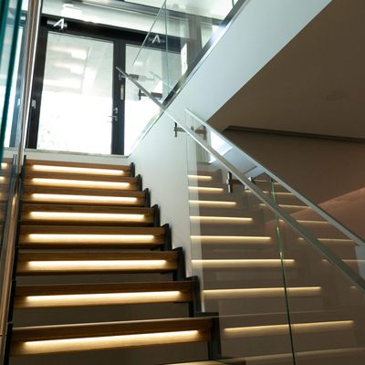 Treppenhausbeleuchtung beleuchtet Glastreppen; moderne LED-Leuchten verstärken die Atmosphäre des Innenraums mit natürlichem Licht darüber.