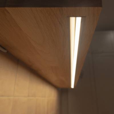 Die LED-Lichtleiste unter dem Holzregal wirft ein indirektes, warmes Licht an die Wand, das sich hervorragend als Akzentbeleuchtung eignet