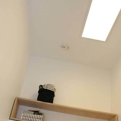 Gemütliches Zimmer mit Holzregal, gestreifter Decke, Korb und Büchern. Eine akzentuierte LED-Deckenleuchte und ein Rauchmelder sorgen für Sicherheit und Stil in einem modernen Zuhause.