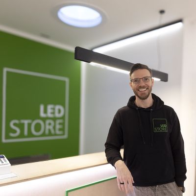 Ein Mann in LED STORE-huvtröja vid belysningsdisk, grüne LED-skylt, moderne Boutique-Umgebung