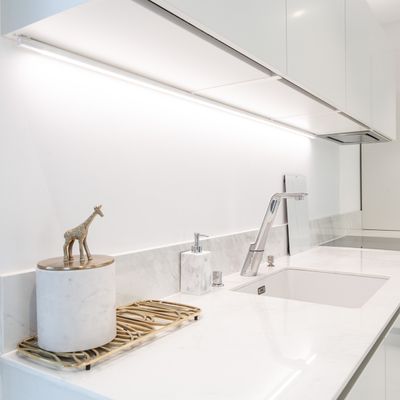Moderne Küche mit weißer Arbeitsplatte, silbernem Wasserhahn, Giraffenfigur im Becken; helle LED-Beleuchtung unter den Schränken für mehr Platz.