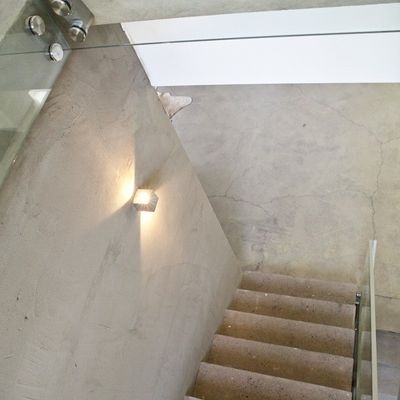Elegante Betontreppe mit LED-Wandleuchte, Glasgeländer und grauem Bodenbelag, der das minimalistische Design in einer modernen Beleuchtungslösung akzentuiert.