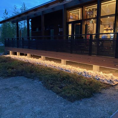 Ein modernes Holzgebäude mit einer LED-beleuchteten Veranda inmitten von Felsen, Dämmerung und Bäumen - für mehr Abendstimmung und Energieeffizienz.
