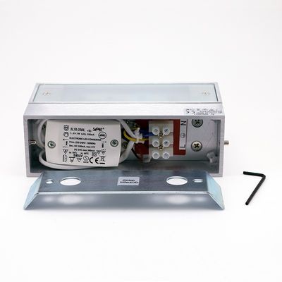 Nahaufnahme einer LED-Beleuchtungskomponente mit sichtbarer Verkabelung, Metallgehäuse und L-förmigem Werkzeug auf weißem Hintergrund für die Elektroinstallation.