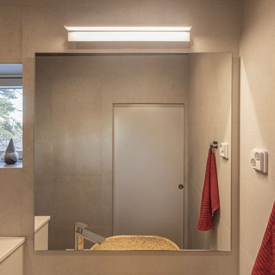 Modernes Badezimmer mit energieeffizienter LED-Beleuchtung, großem Spiegel, beiger Arbeitsplatte, stilvollem Wasserhahn und rotem Handtuchhaken für ein stilvolles Interieur.