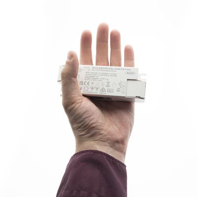 Alternativer Text: Eine Hand hält eine weiße LED-Beleuchtungssteuerung mit Symbolen vor einem klaren Hintergrund, der die technische Innovation von LED-Beleuchtungslösungen hervorhebt.