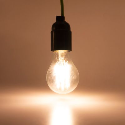 Alternativer Text: LED-Glühbirne leuchtet mit einem warmen Licht, das von der Decke auf einem flachen Hintergrund in einer Leuchtenbewegung hängt.