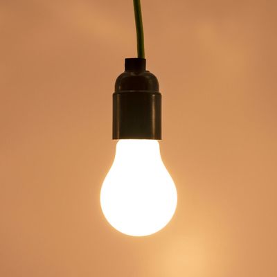 LED-Lampe mit grünem Draht, leuchtet warm vor einem braunen Hintergrund. Ideal für energieeffiziente Beleuchtungslösungen und zur Aufwertung der Atmosphäre.