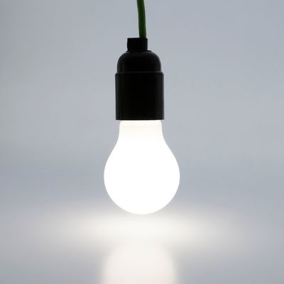 An einem grünen Draht hängende LED-Lampe beleuchtet einen schlichten Hintergrund. Perfekt für energieeffiziente Beleuchtungslösungen.