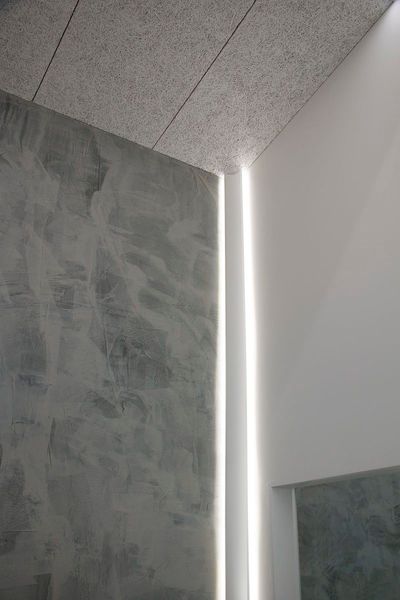 Modernes Eckinterieur mit strukturierten grauen Wänden und vertikalen LED-Lichtleisten; minimalistisch und hell.