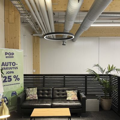 Büro-Lounge mit schwarzem Ledersofa, hölzernem Couchtisch, runder LED-Lampe und Werbebanner auf der linken Seite für eine LED-Beleuchtungsfirma.