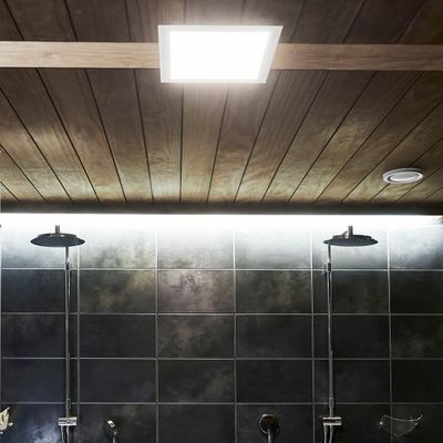 Holzvertäfelte Decke mit LED-Einbauleuchten, die doppelte Duschköpfe an einer elegant gefliesten Badezimmerwand beleuchten.