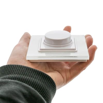 Eine Person hält einen weißen Dimmerschalter auf einem dunkelgrünen Ärmel, der die Steuerung der LED-Beleuchtung vor einem schlichten weißen Hintergrund verbessert.