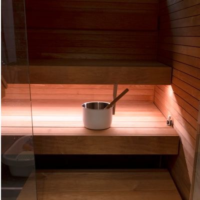 Saunainneneinrichtung aus Holz mit Metalleimer und Schaufel auf den Bänken; warme LED-Beleuchtung zeigt die Gründe für das Holz auf den Sitzflächen.
