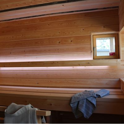 LED-beleuchtete Holzsauna mit Bänken, kleinem Fenster und Handtüchern; perfekte Beleuchtung für ein entspannendes Spa-Erlebnis.