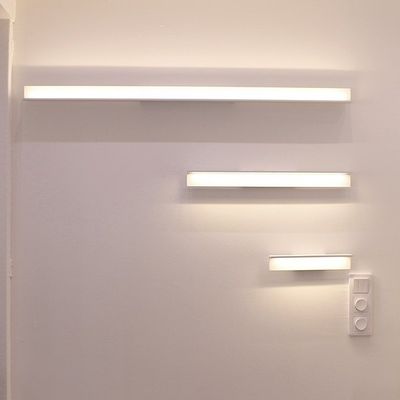 Drei ansteigende Größen von horizontalen, rechteckigen Wandleuchten auf einer weißen Wand, mit einem Lichtschalter unter der kleinsten Leuchte. Modernes LED-Beleuchtungsdesign.