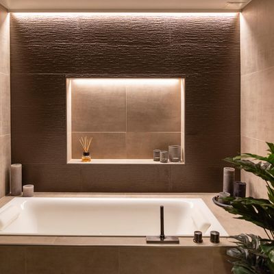 Modernes Badezimmer mit großer eingebauter Badewanne, eingelassenem Regal für Kerzen und Schilfrohrdiffusoren, sanfter LED-Umgebungsbeleuchtung und dekorativer Pflanze.