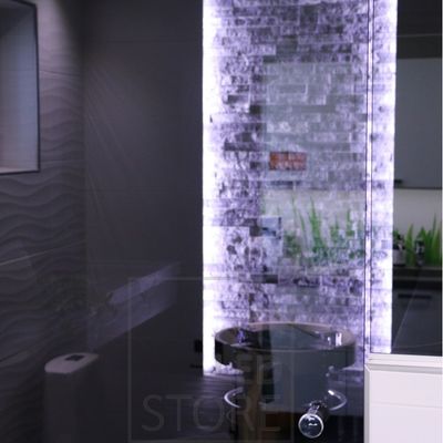 Modernes Bad mit strukturierten Fliesen, hinterleuchteter Wand, rundem Waschbecken und verspiegelten, beleuchteten Fliesen. Elegante LED-Beleuchtung unterstreicht das luxuriöse Design.