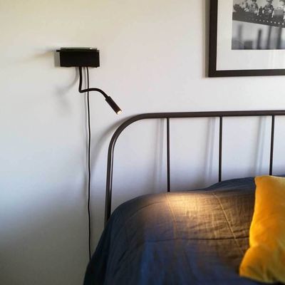 Minimalistisches Schlafzimmer mit wandmontierter LED-Leselampe, Metallbettgestell mit blauer Bettwäsche, gelbem Kissen und einfarbigem Kunstwerk darüber.