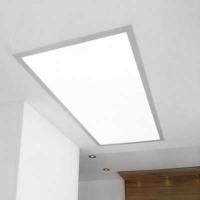 Helle rechteckige LED-Deckenleuchte an einer weißen Decke; brauner Holzakzent in der Ecke für ein modernes Interieur.