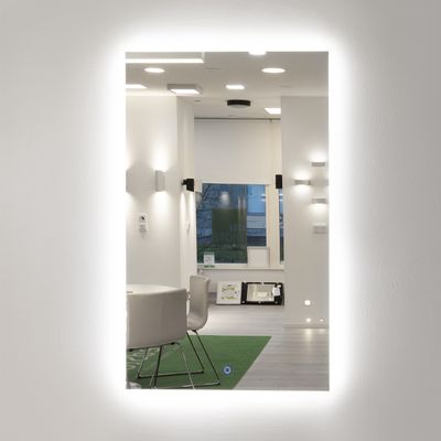 Ein beleuchteter Spiegel, der ein modernes Interieur mit Hängelampen, eleganten Stühlen und natürlichem Licht widerspiegelt.