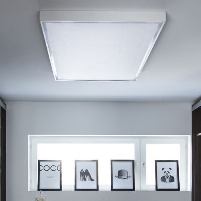 LED-Deckenleuchte beleuchtet monochrom gerahmte Bilder von Text, Schuhen, Hut und Panda auf einem Regal neben einem Fenster in einem modernen Wohnbereich.