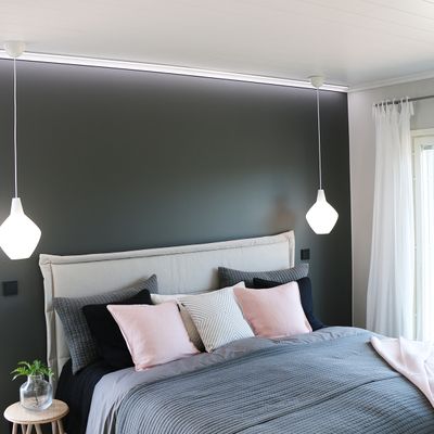 Modernes Schlafzimmer mit grauer Akzentwand, rosa-grauer Bettwäsche, weißen Pendelleuchten und kleinem runden Holztisch mit stilvoller LED-Beleuchtung.
