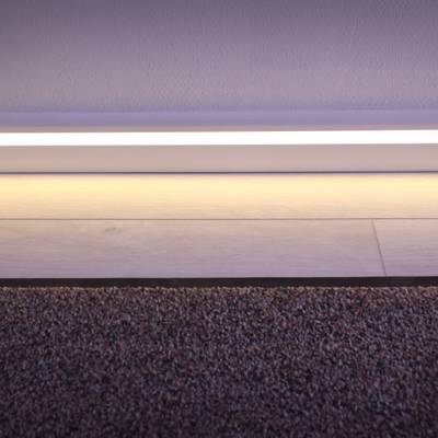 Ein modernes LED-Lichtband beleuchtet den Übergang zwischen Teppich und Holzboden und hebt die weißen Sockeldetails hervor.