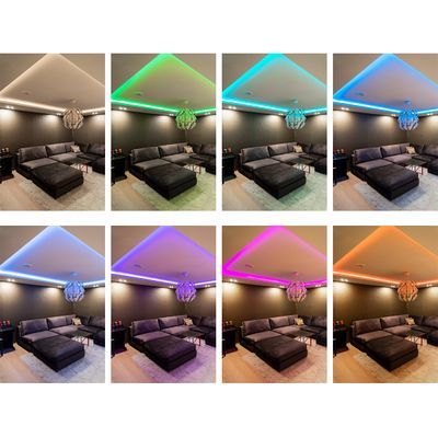 Wohnzimmer mit Querschnittssofa mit acht LED-Deckenleuchten in den Farben: warmweiß, grün, cyan, blau, lila, rosa, magenta. Eine gemütliche Atmosphäre.