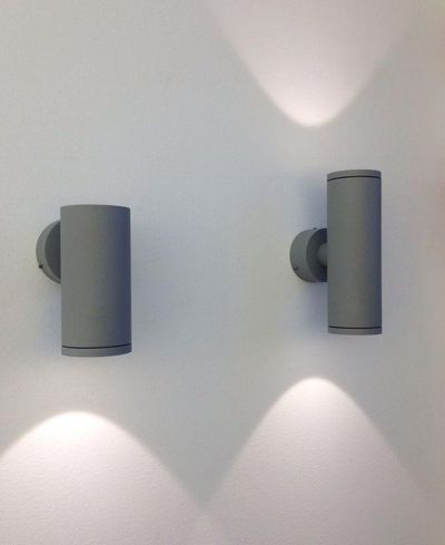 Moderne zylindrische LED-Wandleuchten werfen weiches Licht nach oben und unten auf eine weiße Wand und schaffen so ein stilvolles Ambiente in einem zeitgenössischen Beleuchtungsdesign.