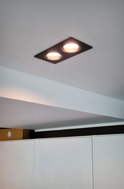 Decke mit zwei rechteckigen LED-Einbauleuchten, die warmes Licht ausstrahlen, Teilansicht der Schränke und des Strahls von unten. Ideal für die moderne Wohnungsbeleuchtung.