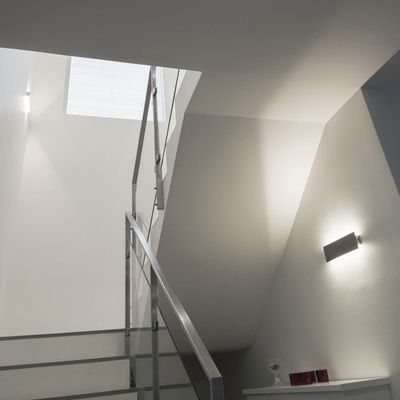 Moderne Treppe mit Metallgeländer, grauen Wänden und LED-Wandbeleuchtung, die zu einem kleinen Fenster darüber führt - energieeffiziente Beleuchtung.
