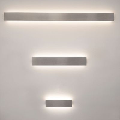 Drei rechteckige, aufrechte LED-Leuchten, die warmes Licht auf eine helle Wand abstrahlen; ideal für moderne Beleuchtungslösungen im Haus.