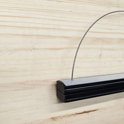 Schwarze Metall-Pendelleuchte mit Metallrahmen vor einer hellen Holzwand in einem LED-Beleuchtungsgeschäft.