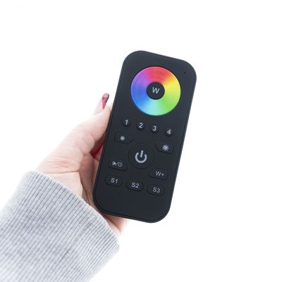 Nahaufnahme einer handgehaltenen, eleganten schwarzen LED-Foto-Fernbedienung mit einem lebhaften Farbrad und mehreren Funktionstasten auf weißem Hintergrund.