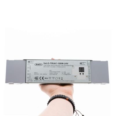 Nahaufnahme einer Hand, die den VaLO TRIAC-100W-24V LED-Dimmer mit Digitalanzeige hält, der die Energieeffizienz von LED-Beleuchtung verbessert.