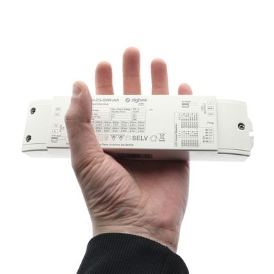 In der Hand ein weißes, rechteckiges Gerät mit technischen Informationen und Symbolen sowie dem Wort "Zigbee" im Zusammenhang mit der LED-Beleuchtungstechnologie.